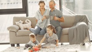Cheerful family wearing casual clothes sitting in living room while playing and drinking tea during weekend at home in morning